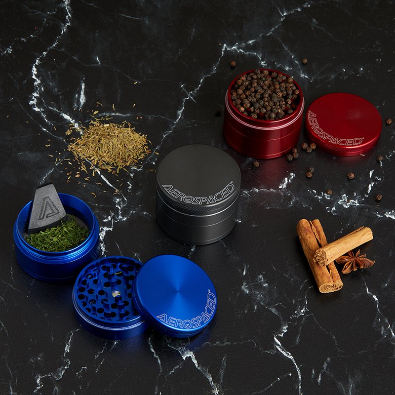 Blue, graphite and red AEROSPACED 4-piece grinders on black marble with peppercorns, cinnamon and star anise